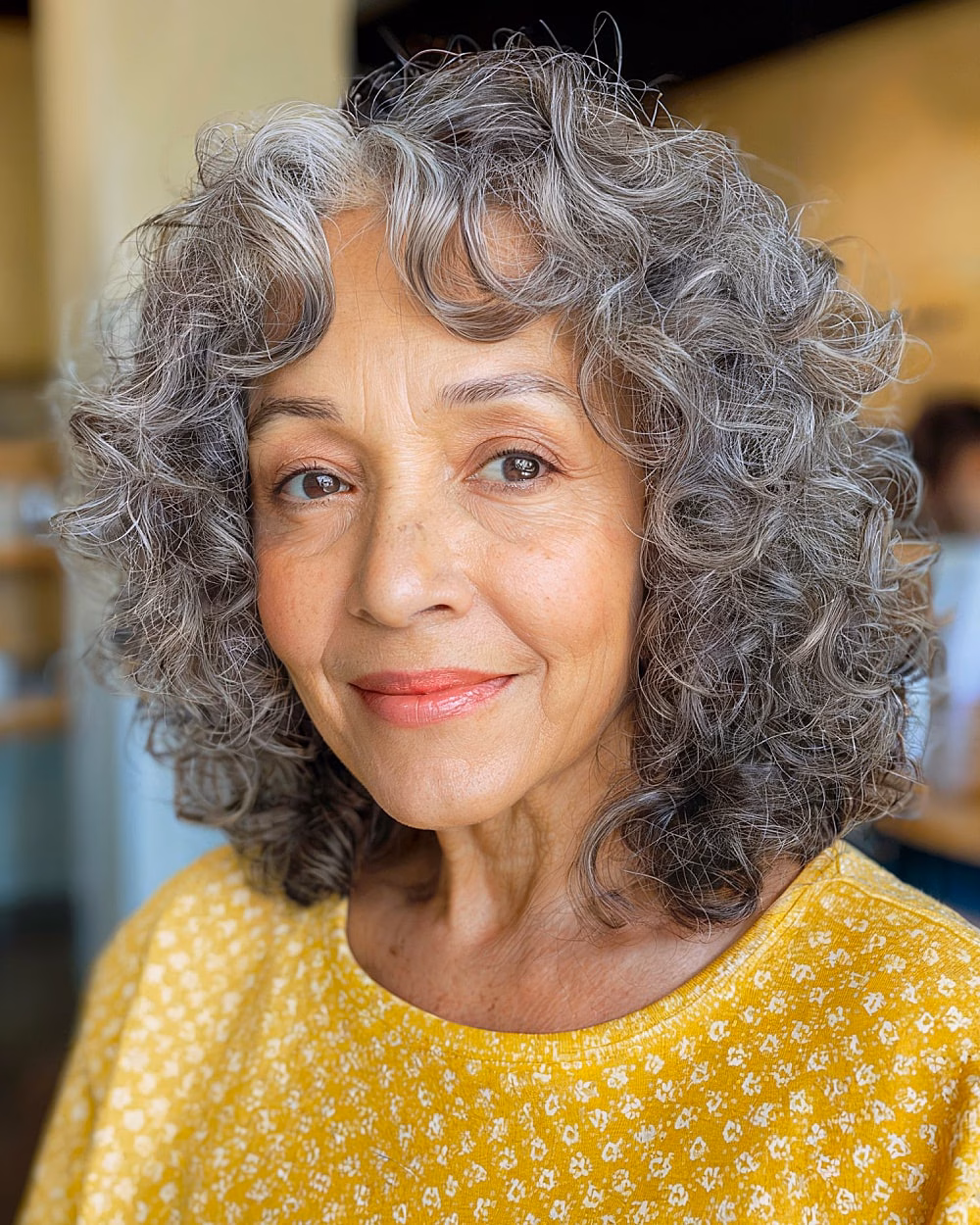 Naturally curly salt and pepper hair with curtain bangs adding softness and shape over 70