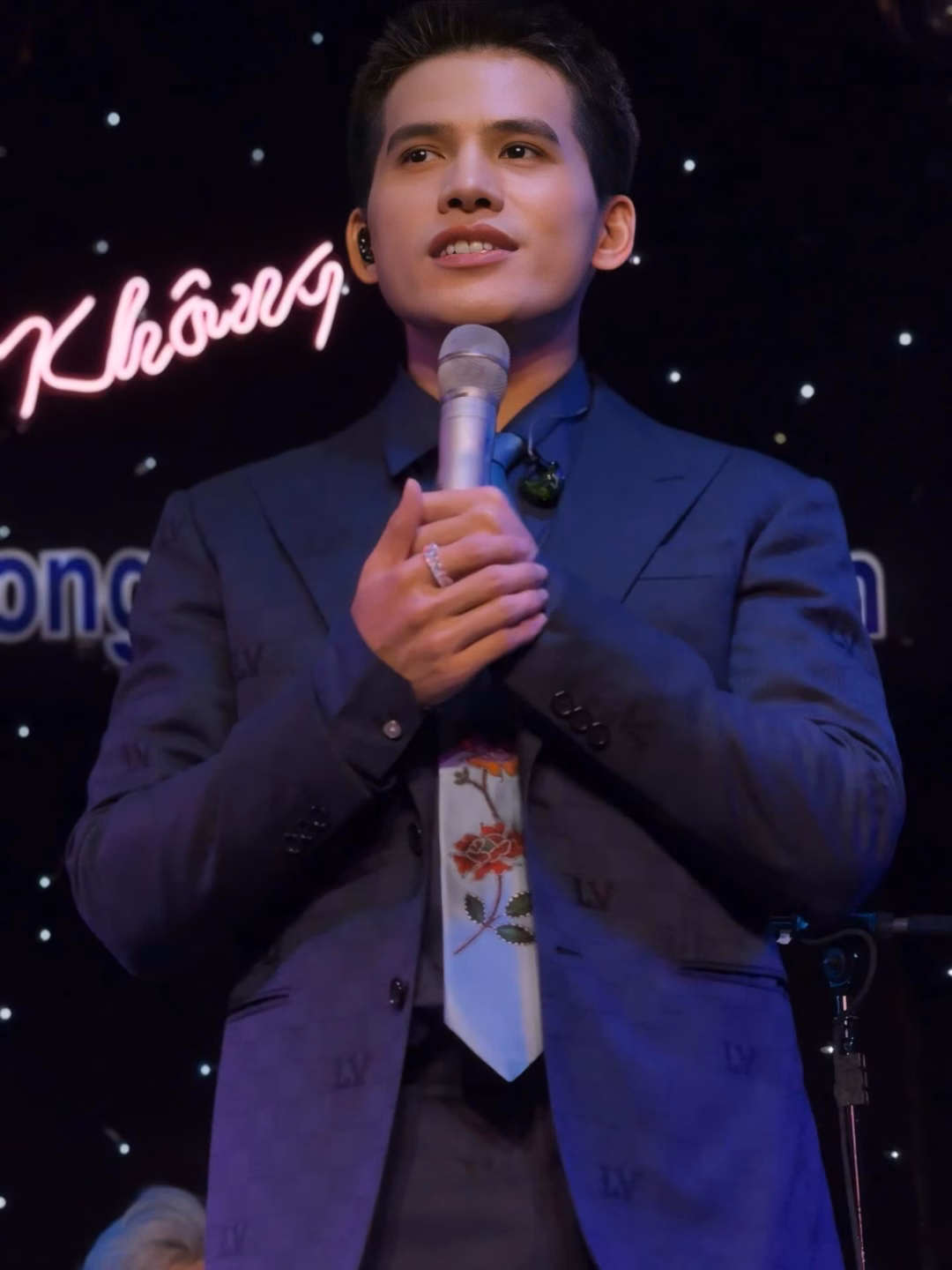 May be an image of 1 person, microphone, dinner jacket, concert and text that says 'Không n'