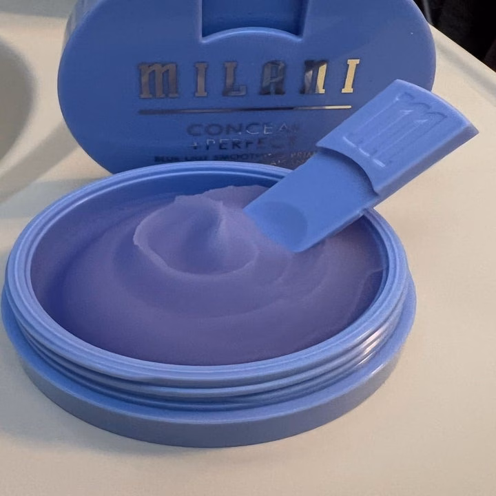 Mascara giúp mi dài và volum hóa bền lâu chỉ với dầu jojoba Milani makeup concealer in an open container, showing a creamy texture with a small spatula on the lid