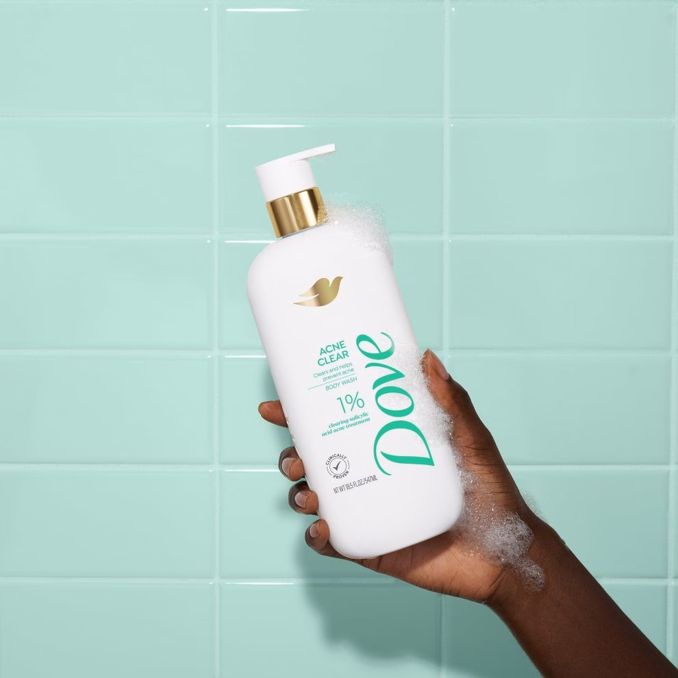 3 sản phẩm chăm sóc da giúp giảm đỏ và làm dịu kích ứng hiệu quả Hand holding a Dove Acne Clear Body Cleanser bottle with foam against a tiled background