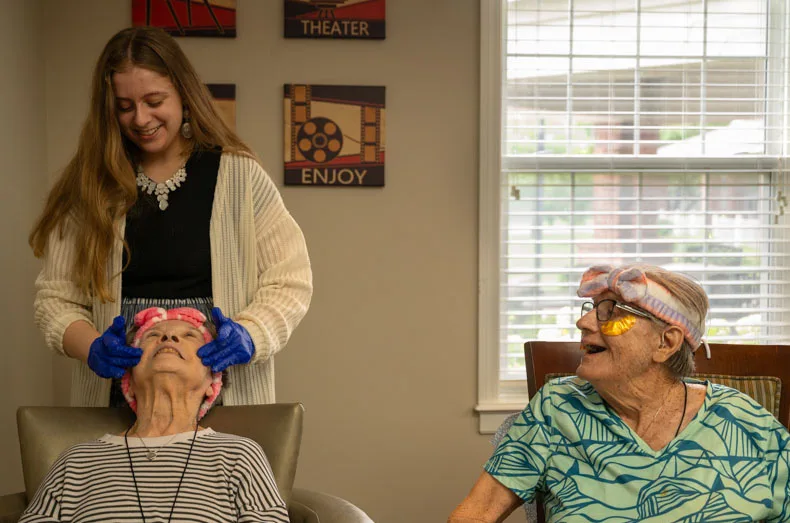 Cheyenne McNish applies lotion on Charlotte while fellow resident and friend Jenny watches on. Amanda and Cheyenne are a mother-and-daughter pair who bond through their work and the connections they make with residents. Photo credit Julian Schnittker.
