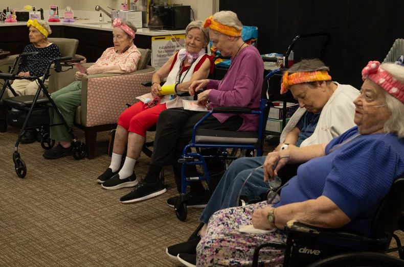 Assisted living residents attending Gorgeous Grandmas Day wait their turn for a facial and makeup, already sporting salon-style headbands and personalized gift bags. Residents received bracelets, affirmation cards, and more in their gift bags. Photo credit Julian Schnittker.
