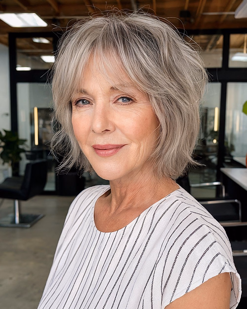 Silver tousled bob with textured layers and curtain bangs for volume and movement over 70