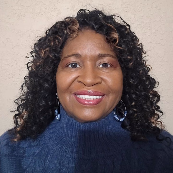 Smiling person with curly hair wearing a textured turtleneck sweater and dangling earrings