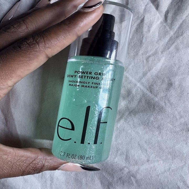Hand holding e.l.f. Power Grip Dewy Setting Spray bottle, labeled as "shockingly fine."