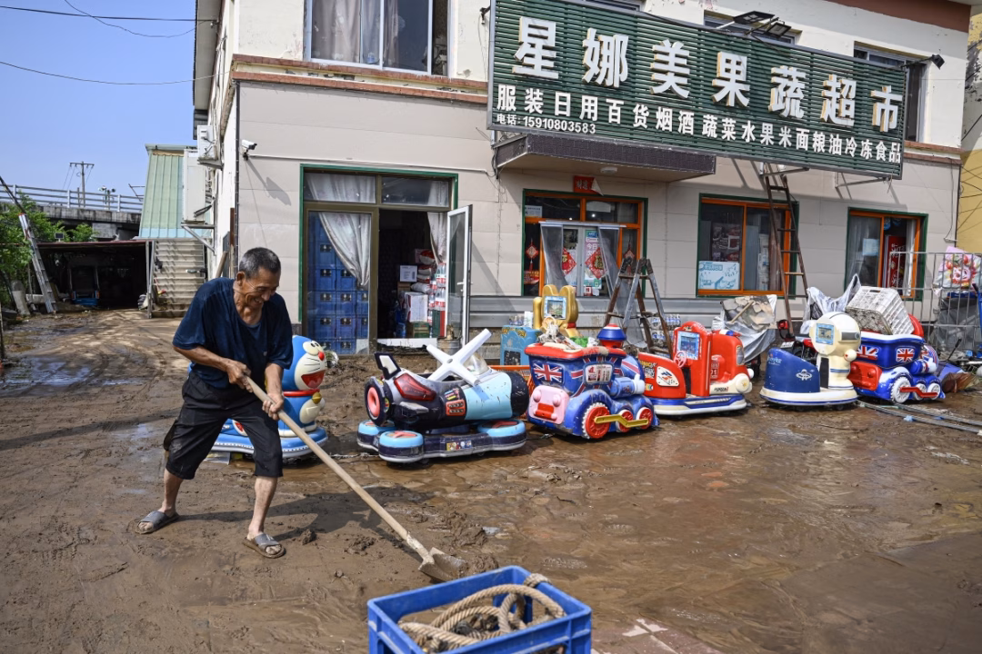 Lụt lớn ở Bắc Kinh, 30 người chết và hàng nghìn người phải sơ tán Người đàn ông dọn dẹp bùn đất trước siêu thị.