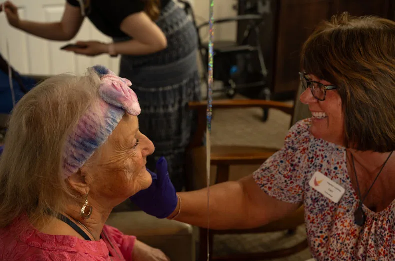 Lisa, a concierge at Pegasus Landing, laughs along with resident Kay as she applies lotion. “I’ve never had such a good [makeup] job,” said Kay. Photo credit Julian Schnittker.
