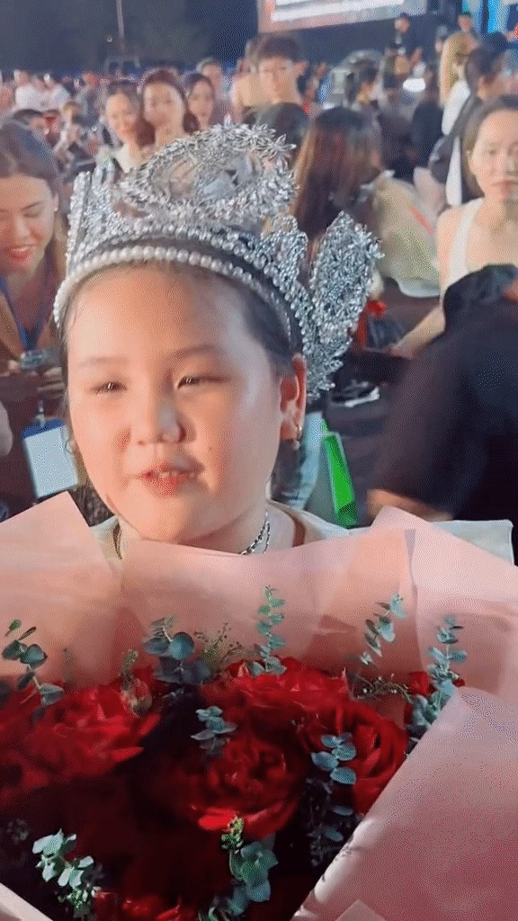 Em gái Ý Nhi ôm hoa đội vương miện và trả lời phỏng vấn sau khi chị gái đăng quang.