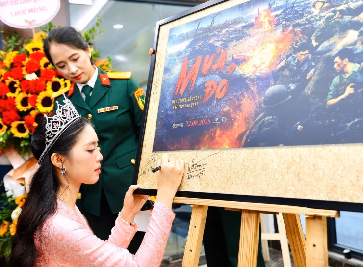 Á hậu Trần Ngọc Châu Anh rạng rỡ trong lễ khai mạc triển lãm ảnh Mưa đỏ Người đẹp ký vào poster quảng bá bộ phim.