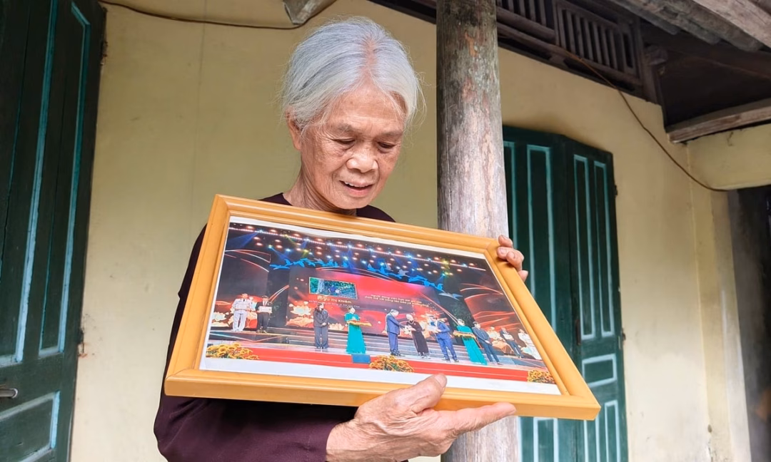 Bà Vũ Thị Khiêm bên tấm ảnh được Tổng Bí thư Tô Lâm tặng danh hiệu Người đảng viên trọn đời giữ lửa đam mê với công tác bảo vệ môi trường. Ảnh: Phạm Hiếu.