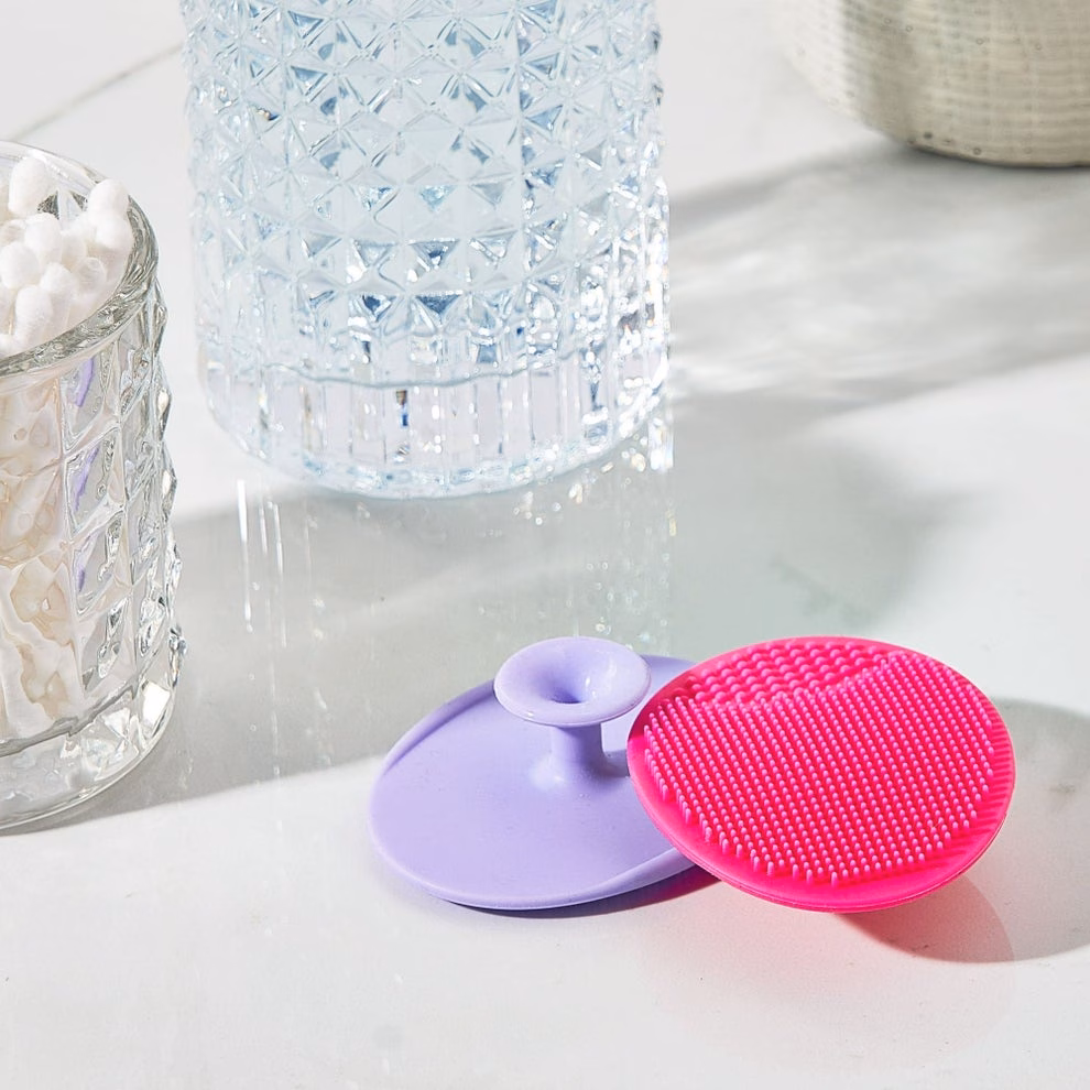 Facial cleansing pads with textured surfaces placed on a bathroom counter next to a glass container