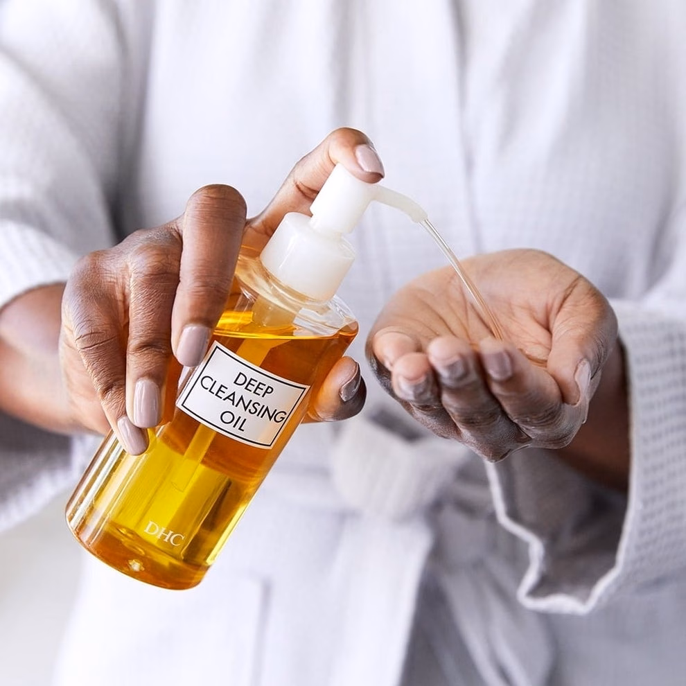Person in a robe uses a pump bottle labeled &quot;Deep Cleansing Oil&quot; to dispense oil into their hand