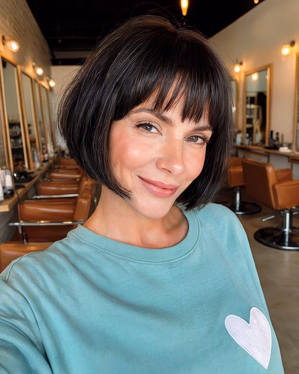 Short black bob haircut with fringe on thick straight hair in a salon setting
