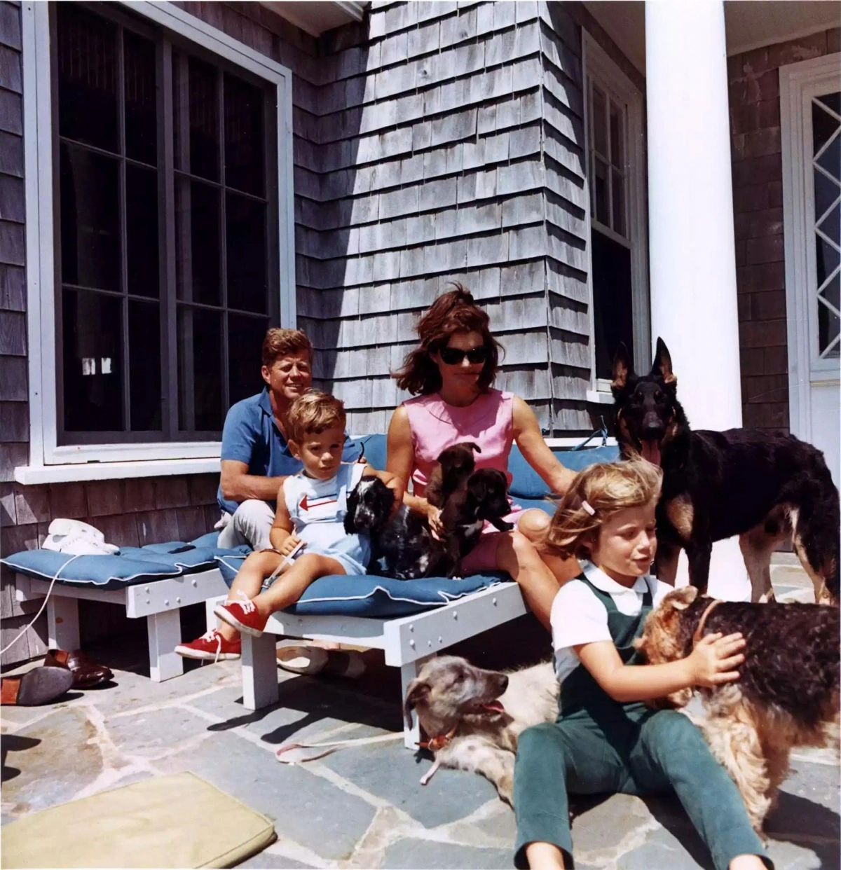 Phong cách bất hủ của Jackie Kennedy: Biểu tượng vẻ đẹp và trí tuệ của Đệ nhất Phu nhân Mỹ Tại khu nhà nghỉ Kennedy ở Hyannis Port, bang Massachusetts, bà Jackie xuất hiện trong khung cảnh ấm áp bên em chồng Robert và hai con là Caroline và John Jr. Bao quanh họ là những chú chó cưng, gợi lên hình ảnh một mái ấm yên bình và giản dị.