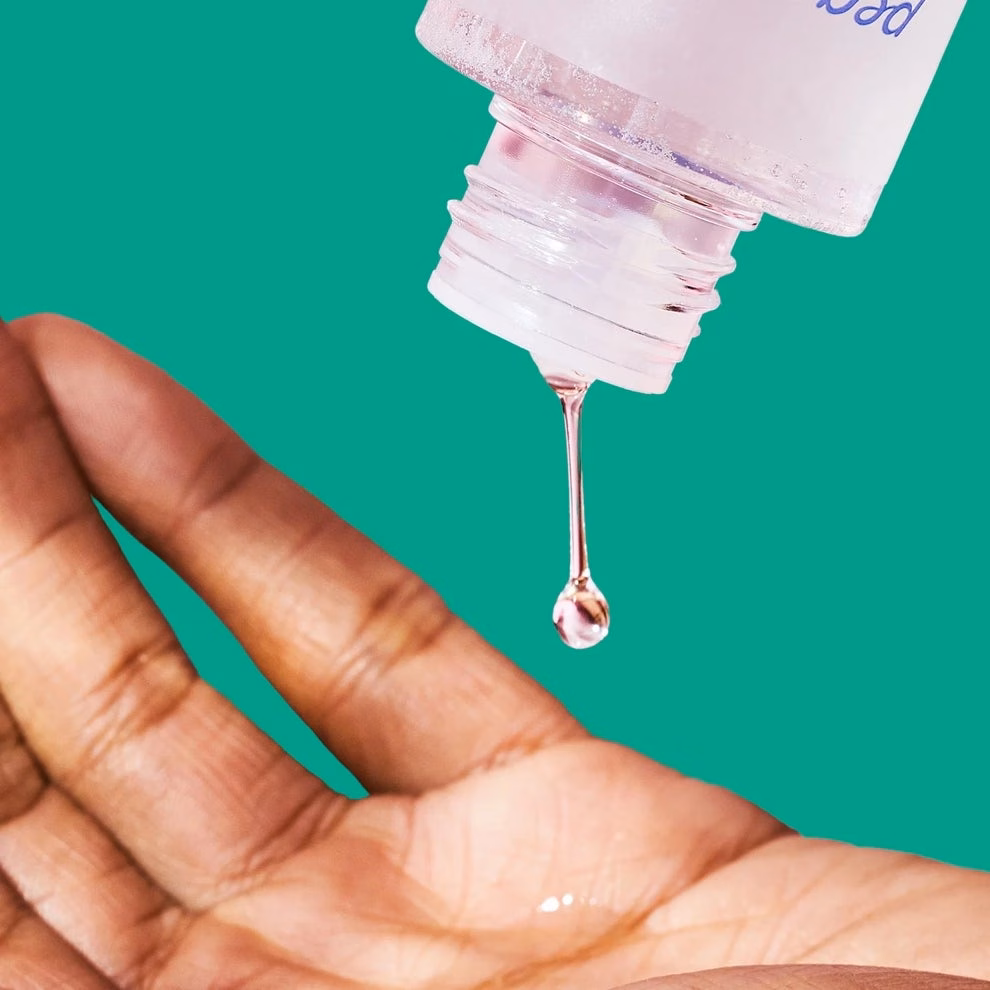 3 Sản Phẩm Làm Đẹp Hiệu Quả Giúp Cải Thiện Làn Da Hand with clear liquid bottle dispensing a drop, suggesting skincare or hygiene product application
