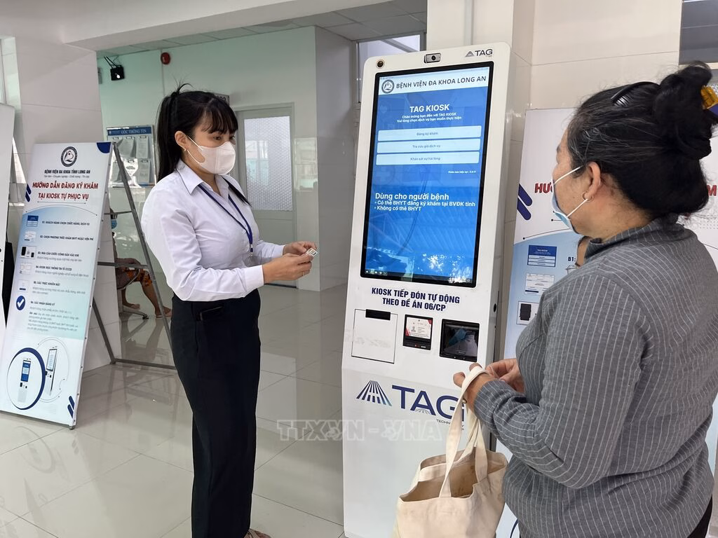 Nhân viên Bệnh viện đa khoa Long An hướng dẫn người dân sử dụng Kiosk tự phục vụ - đăng ký khám chữa bệnh qua máy tự động.