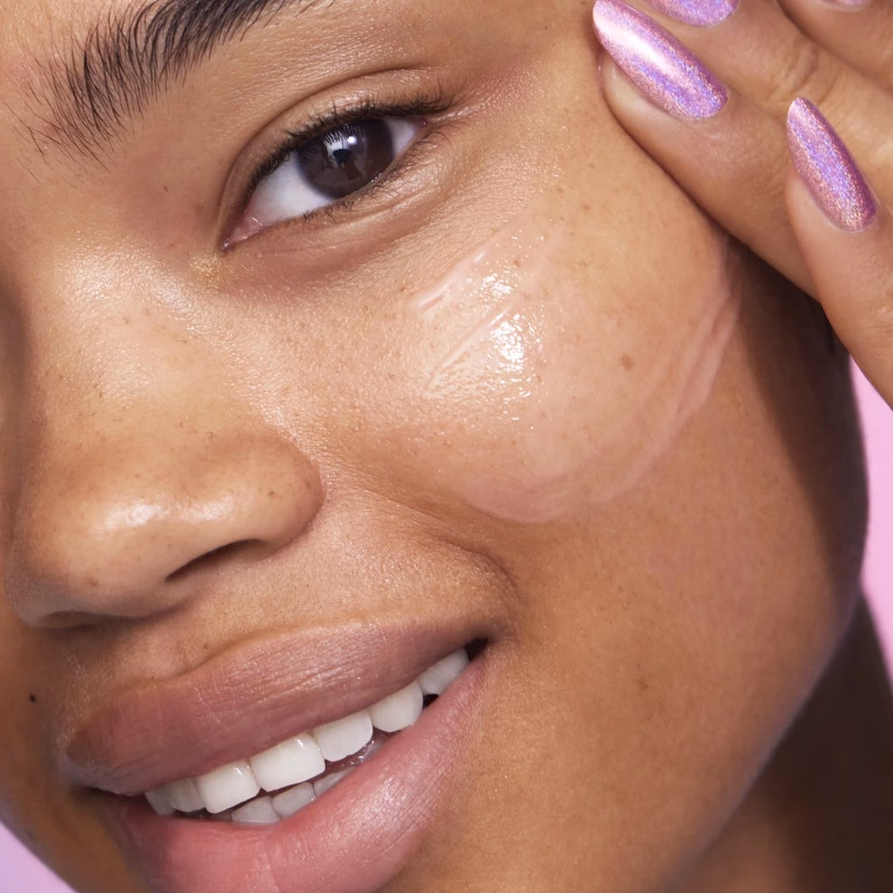 3 sản phẩm skincare ‘hot’ giúp điều trị mụn, dưỡng da mịn màng Person applying skincare cream to face, showcasing smooth complexion and polished nails, suitable for a shopping article on beauty products