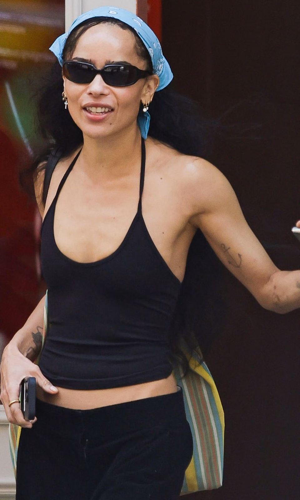 Sao nữ Hollywood đua nhau khoe phong cách minimalist chic hè này Zoe Kravitz flashes a smile while stepping out in New York City. The American actress carried a large striped tote bag and wore a bandana, black tank top, matching trousers, and sandals.
