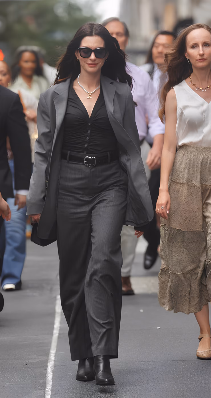 Anne Hathaway năng động và hiện đại khi diện set đồ vest màu xám, xách cặp Coach 895 USD, mang boots Golden Goose, đeo vòng cổ kim cương Jemma Wynne 14.910 USD.