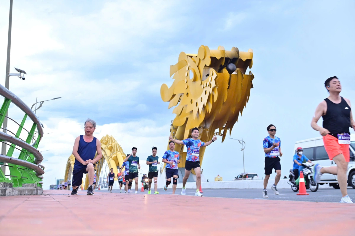VĐV Huỳnh Anh Khôi vô địch VnExpress Marathon Đà Nẵng cự ly 42km 7h, đông đảo VĐV 10km chinh phục cầu Rồng. Trên vỉa hè, nhiều người dân tập thể dục buổi sáng.